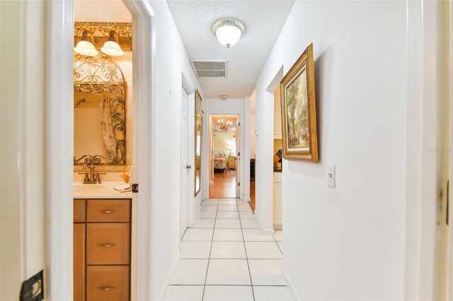 corridor with a textured ceiling, light tile patterned floors, and sink