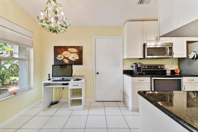 kitchen with dark stone countertops, light tile patterned floors, appliances with stainless steel finishes, white cabinets, and a chandelier