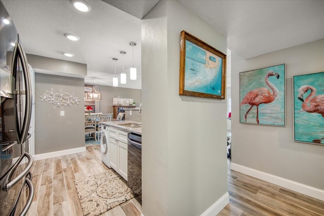 kitchen featuring white cabinets, light hardwood / wood-style floors, decorative light fixtures, and stainless steel refrigerator