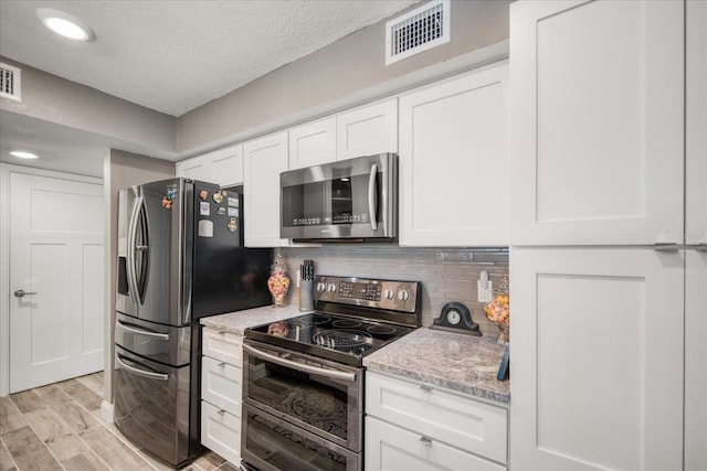 kitchen featuring light wood-type flooring, white cabinetry, backsplash, appliances with stainless steel finishes, and light stone counters