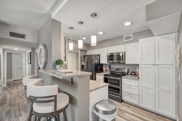 kitchen featuring stainless steel appliances, decorative light fixtures, light wood-type flooring, and white cabinetry