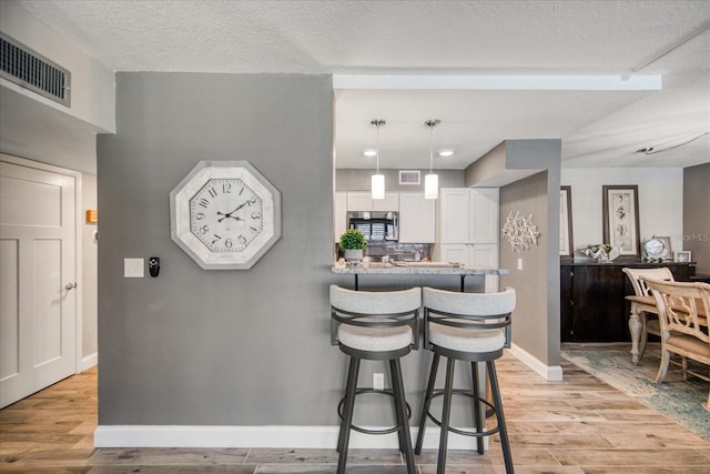 kitchen with a textured ceiling, white cabinets, a breakfast bar area, light hardwood / wood-style flooring, and kitchen peninsula