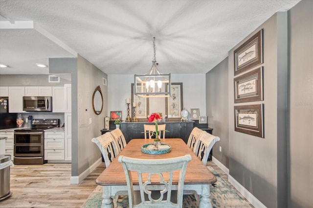 dining room featuring an inviting chandelier, light hardwood / wood-style flooring, and a textured ceiling