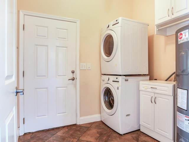 clothes washing area with water heater, dark tile patterned floors, cabinets, and stacked washer and clothes dryer