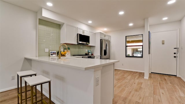 kitchen featuring white cabinets, tasteful backsplash, light wood-type flooring, stainless steel appliances, and a kitchen breakfast bar