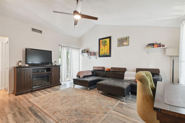 living room featuring lofted ceiling, light hardwood / wood-style floors, ceiling fan, and a textured ceiling