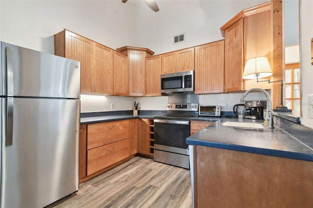 kitchen with light wood-type flooring, appliances with stainless steel finishes, a towering ceiling, sink, and ceiling fan