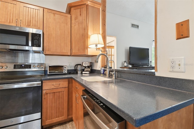 kitchen with sink, appliances with stainless steel finishes, kitchen peninsula, and light hardwood / wood-style floors