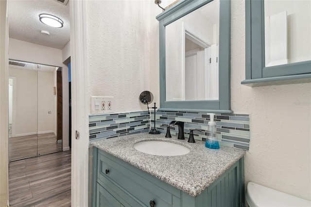 bathroom with a textured ceiling, oversized vanity, tasteful backsplash, toilet, and wood-type flooring