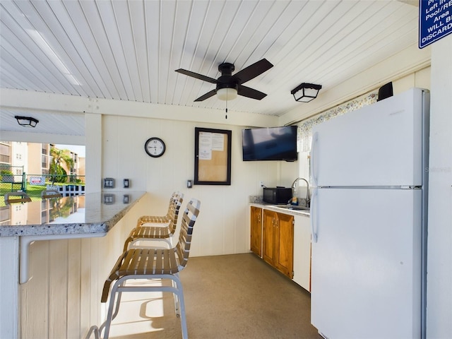 kitchen with a kitchen breakfast bar, kitchen peninsula, white fridge, sink, and ceiling fan