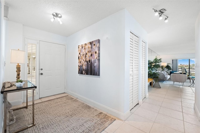 foyer entrance featuring a textured ceiling, track lighting, and light tile patterned floors