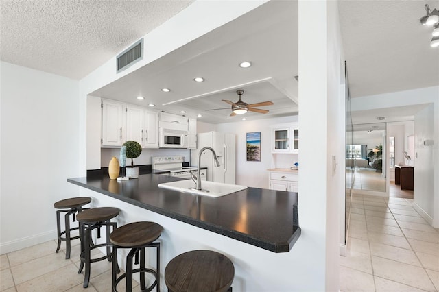 kitchen featuring a textured ceiling, white cabinets, kitchen peninsula, a kitchen bar, and white appliances