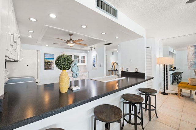 kitchen featuring a breakfast bar, sink, white cabinets, kitchen peninsula, and a raised ceiling