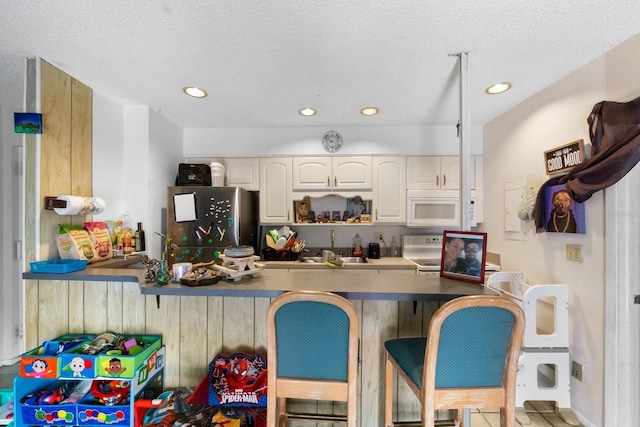 kitchen featuring a breakfast bar area, a textured ceiling, white appliances, and white cabinetry