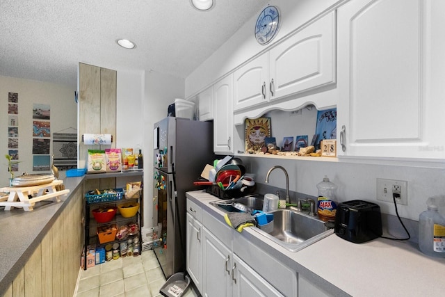 kitchen featuring light tile floors, a textured ceiling, sink, stainless steel refrigerator, and white cabinetry