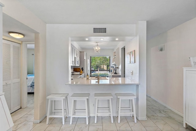 kitchen featuring light tile floors, kitchen peninsula, a breakfast bar, and white cabinetry