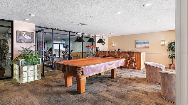 game room with a textured ceiling, pool table, carpet floors, and bar area