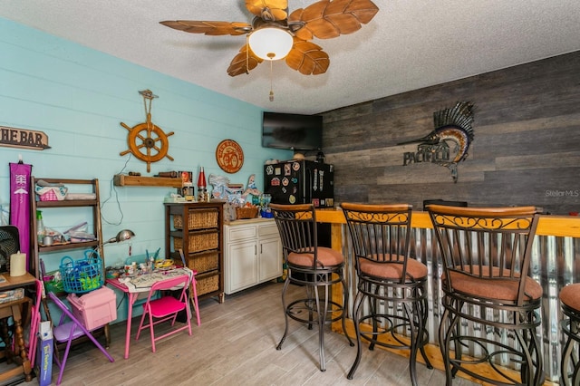 interior space featuring wooden walls, light hardwood / wood-style floors, ceiling fan, and a textured ceiling