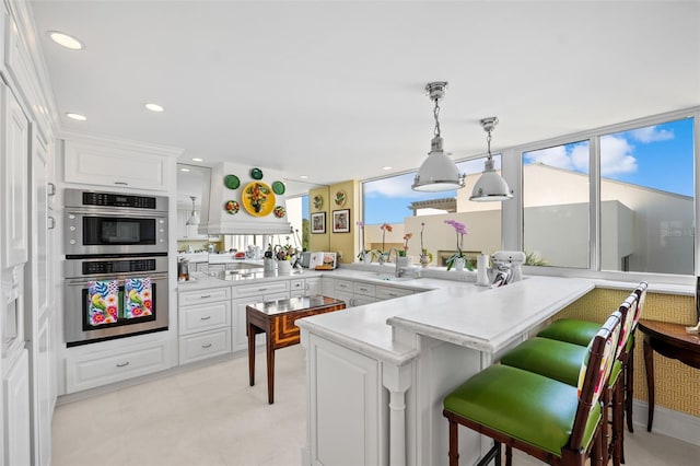 kitchen with a kitchen breakfast bar, kitchen peninsula, white cabinets, pendant lighting, and stainless steel double oven