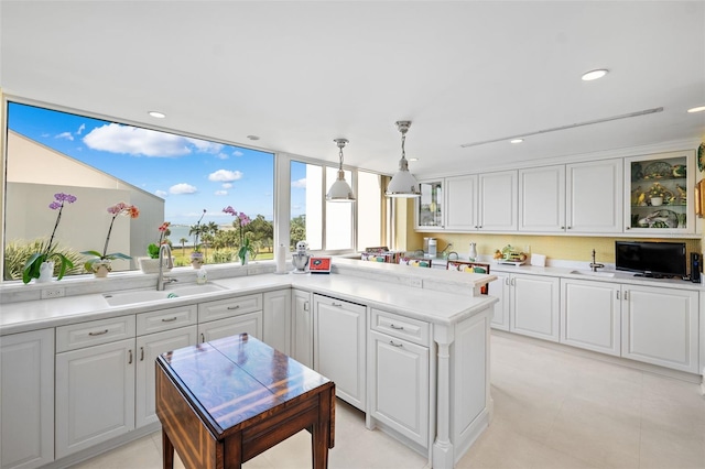 kitchen with light tile flooring, pendant lighting, backsplash, sink, and white cabinets