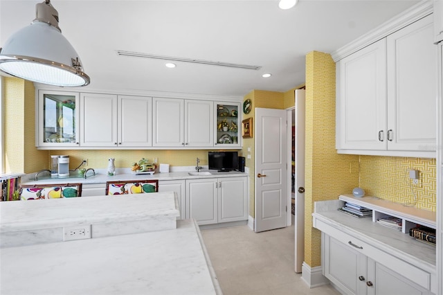 kitchen with light stone counters, white cabinets, sink, and light tile floors