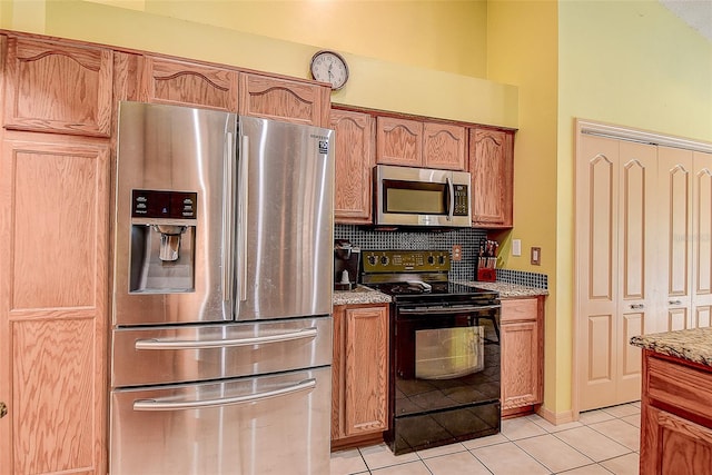 kitchen with light stone countertops, stainless steel appliances, light tile flooring, and backsplash