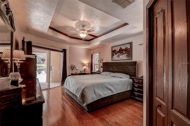 bedroom featuring access to outside, a tray ceiling, dark wood-type flooring, and multiple windows