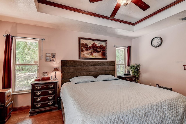 bedroom with a tray ceiling, ceiling fan, dark hardwood / wood-style floors, and multiple windows