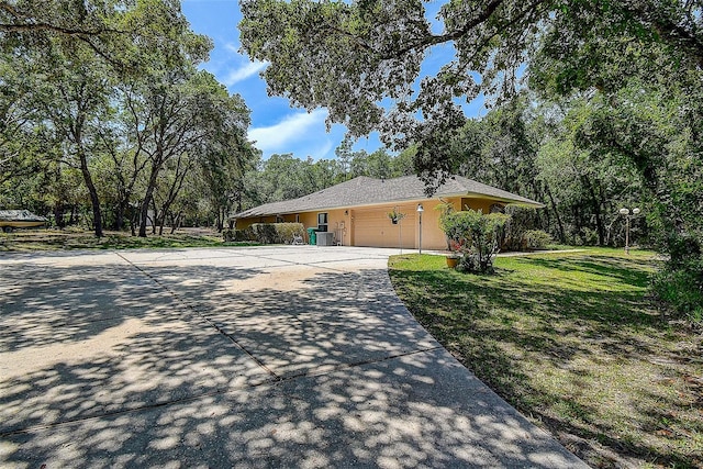 view of side of home featuring stucco siding, driveway, central AC, a yard, and a garage