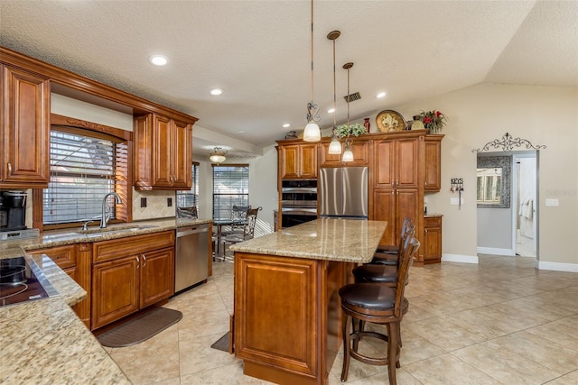 kitchen with sink, vaulted ceiling, appliances with stainless steel finishes, a kitchen island, and pendant lighting