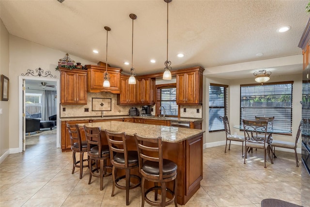 kitchen featuring a kitchen island, pendant lighting, tasteful backsplash, sink, and light stone countertops