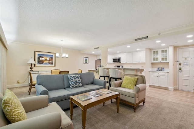 living room featuring ornamental molding, a notable chandelier, light hardwood / wood-style floors, and a textured ceiling