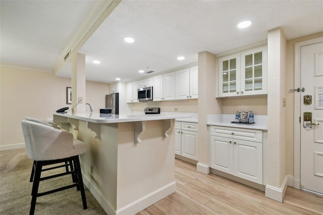 kitchen with appliances with stainless steel finishes, a kitchen breakfast bar, light wood-type flooring, and white cabinets