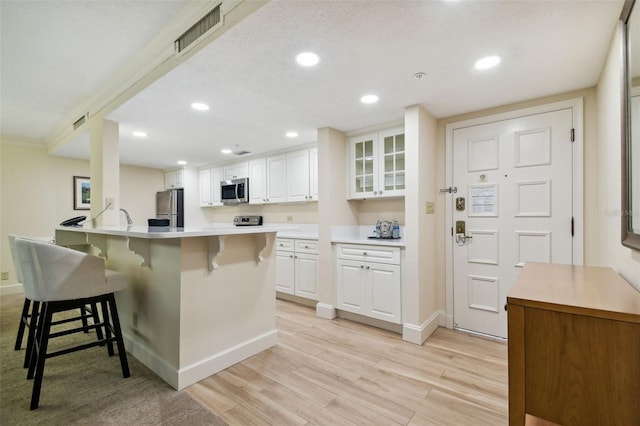 kitchen featuring a kitchen breakfast bar, stainless steel appliances, light hardwood / wood-style floors, and white cabinetry