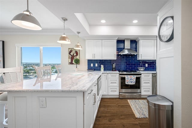 kitchen featuring white cabinets, hanging light fixtures, wall chimney exhaust hood, appliances with stainless steel finishes, and kitchen peninsula