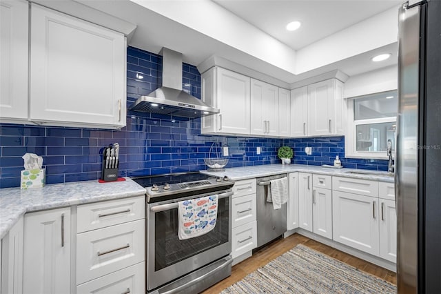 kitchen with white cabinets, wall chimney range hood, stainless steel appliances, and tasteful backsplash