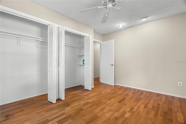 unfurnished bedroom with hardwood / wood-style flooring, ceiling fan, a textured ceiling, and multiple closets