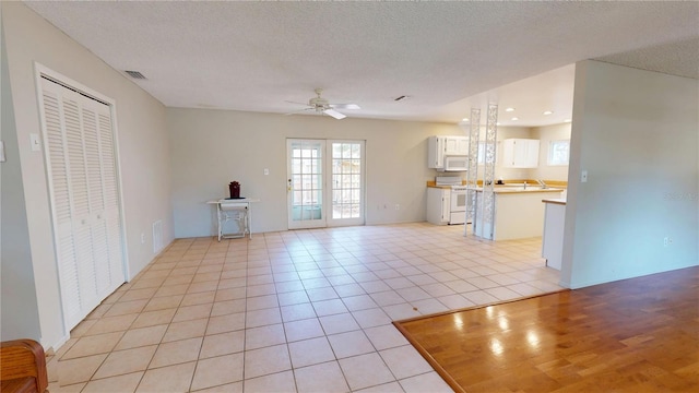 unfurnished living room with light tile patterned floors, visible vents, a ceiling fan, a textured ceiling, and french doors