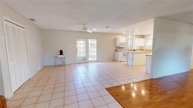 unfurnished living room with a textured ceiling, light tile patterned flooring, visible vents, and a ceiling fan