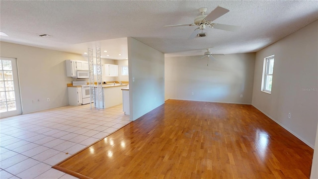 unfurnished living room with a healthy amount of sunlight, light wood-style flooring, visible vents, and a textured ceiling