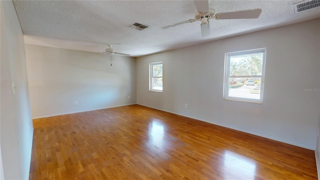 unfurnished room featuring a textured ceiling, wood finished floors, visible vents, and a ceiling fan