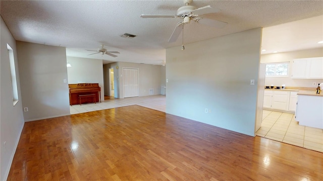 unfurnished living room featuring a ceiling fan, light wood-type flooring, visible vents, and a textured ceiling