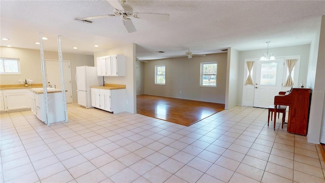 kitchen featuring light countertops, freestanding refrigerator, open floor plan, white cabinets, and a textured ceiling