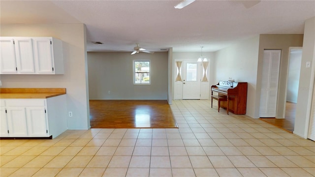 kitchen featuring light tile patterned floors, ceiling fan with notable chandelier, white cabinets, and open floor plan