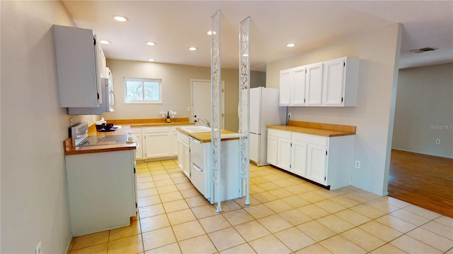 kitchen featuring a kitchen island with sink, a sink, visible vents, white cabinetry, and freestanding refrigerator