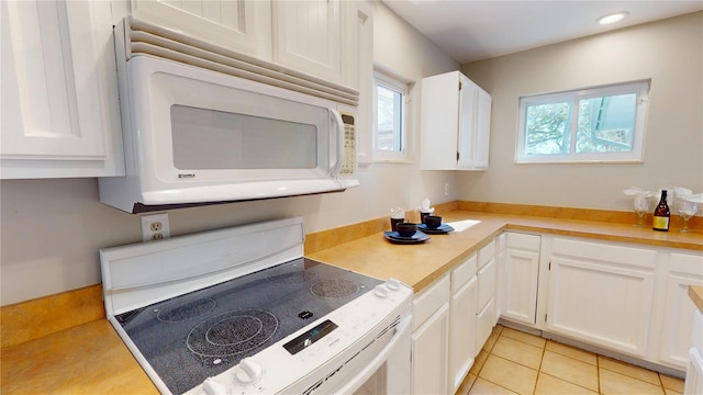 kitchen featuring light tile patterned floors, electric stove, white microwave, light countertops, and white cabinetry