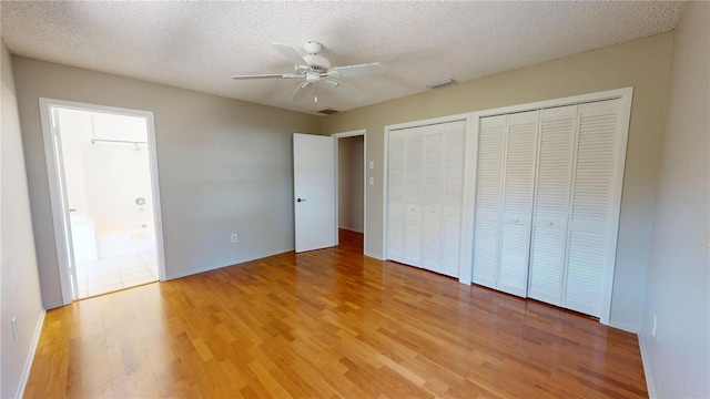 unfurnished bedroom with multiple closets, visible vents, a textured ceiling, and light wood finished floors