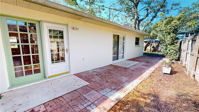 view of exterior entry featuring fence, a patio, and stucco siding