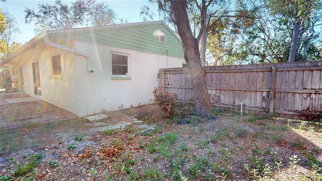 view of side of home featuring stucco siding, fence, and a patio