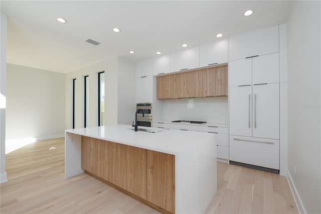 kitchen featuring cooktop, white cabinetry, a kitchen island with sink, and light hardwood / wood-style flooring